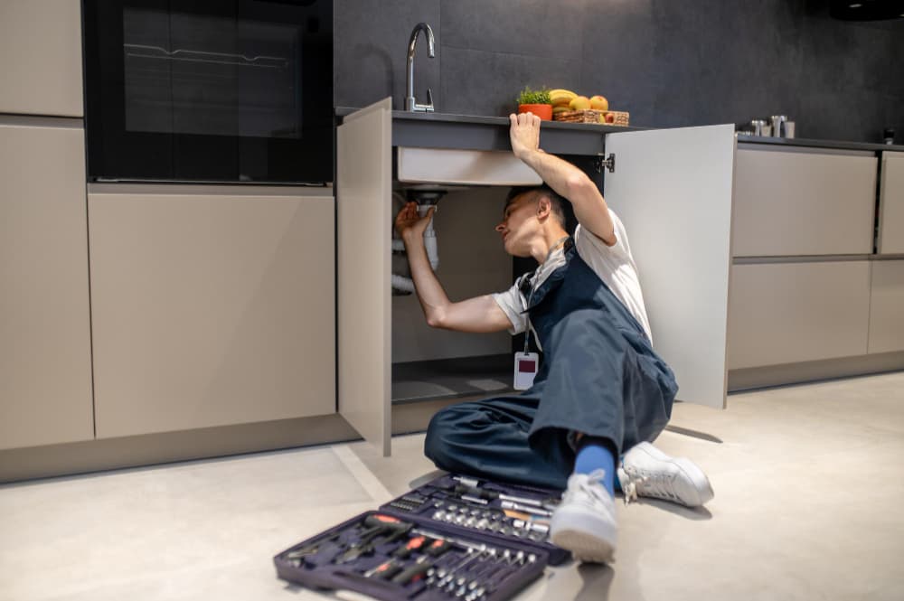 RJC plumber working on kitchen plumbing beneath a sink cabinet