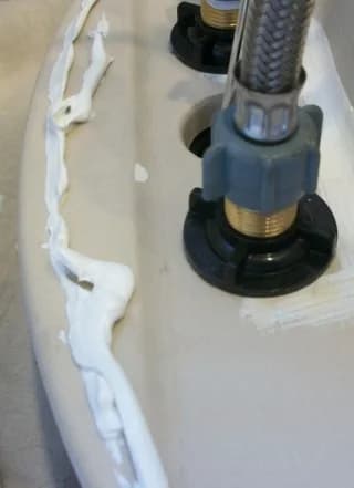 Plumber applying caulk along the underside edge of a bathroom sink during installation