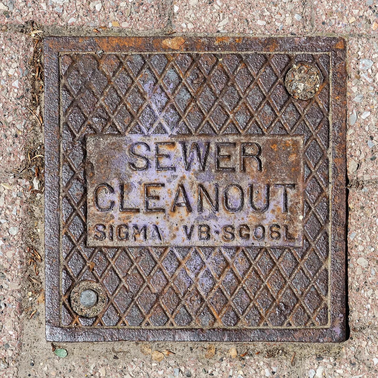 Cast-iron sewer cleanout access cover set in a paved outdoor walkway