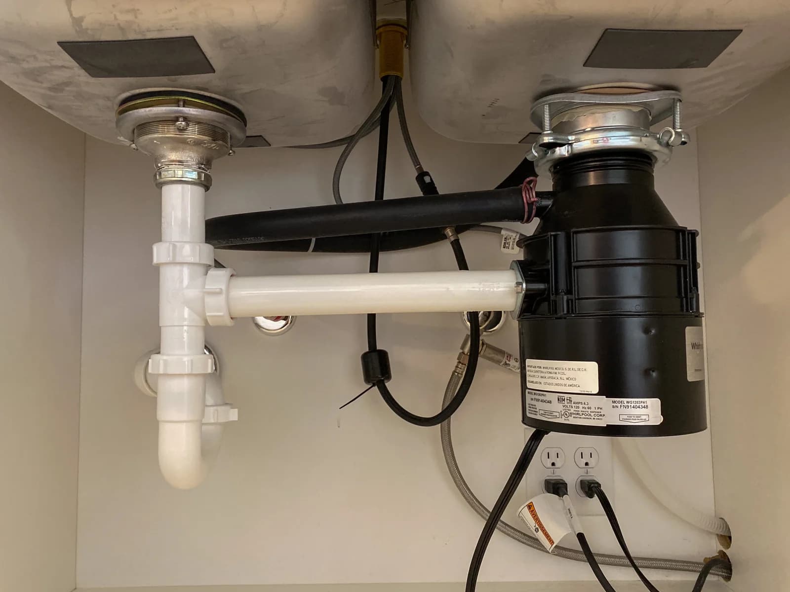 Garbage disposal unit mounted under a double kitchen sink with white PVC trap and drain piping
