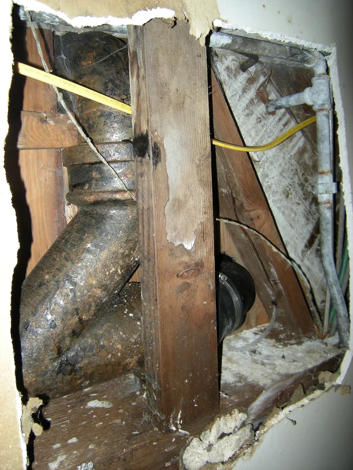 Cast-iron drain-waste-vent fitting exposed inside an opened wall between wood studs