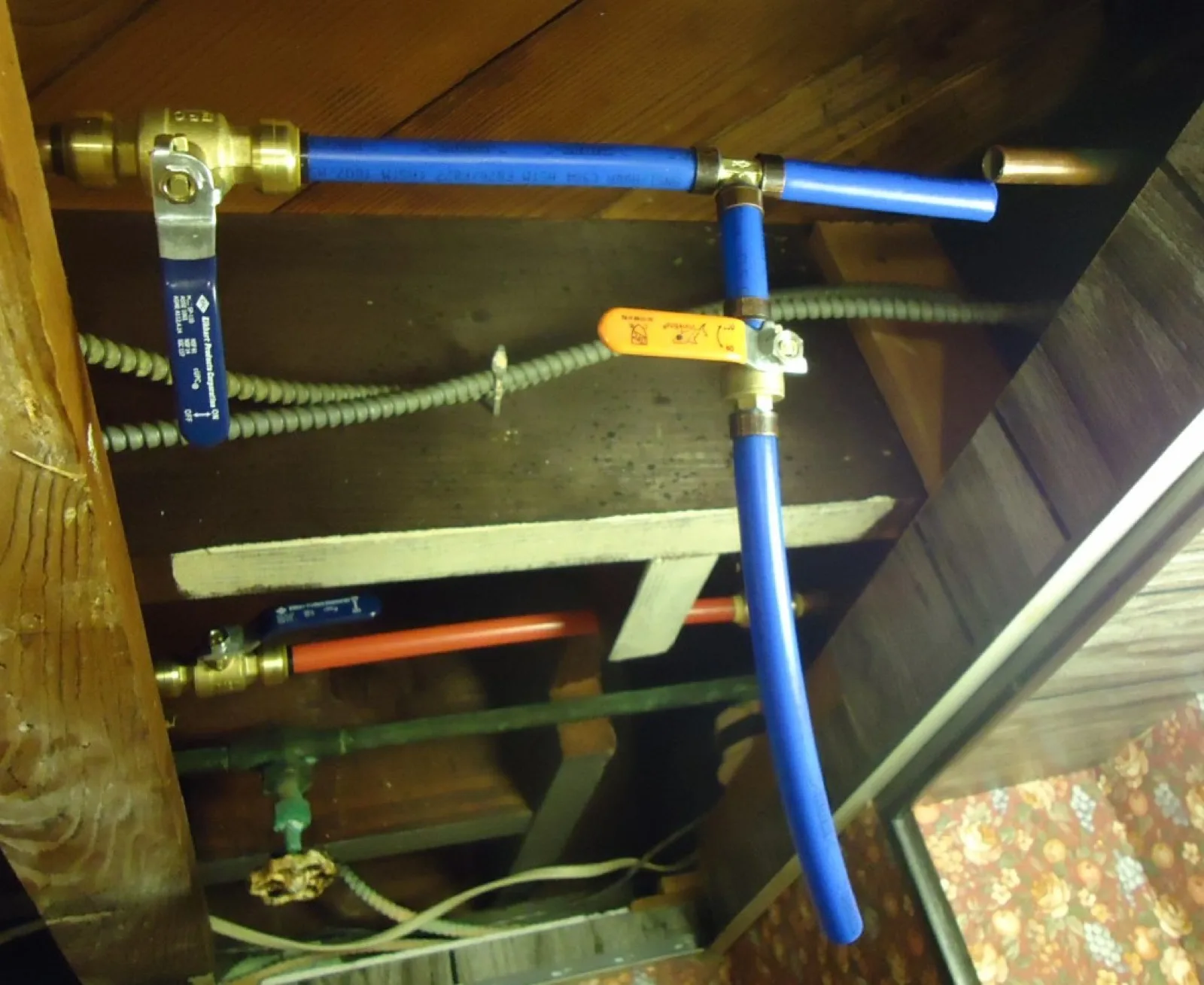 Red and blue PEX tubing running along a basement ceiling with ball-valve shutoffs