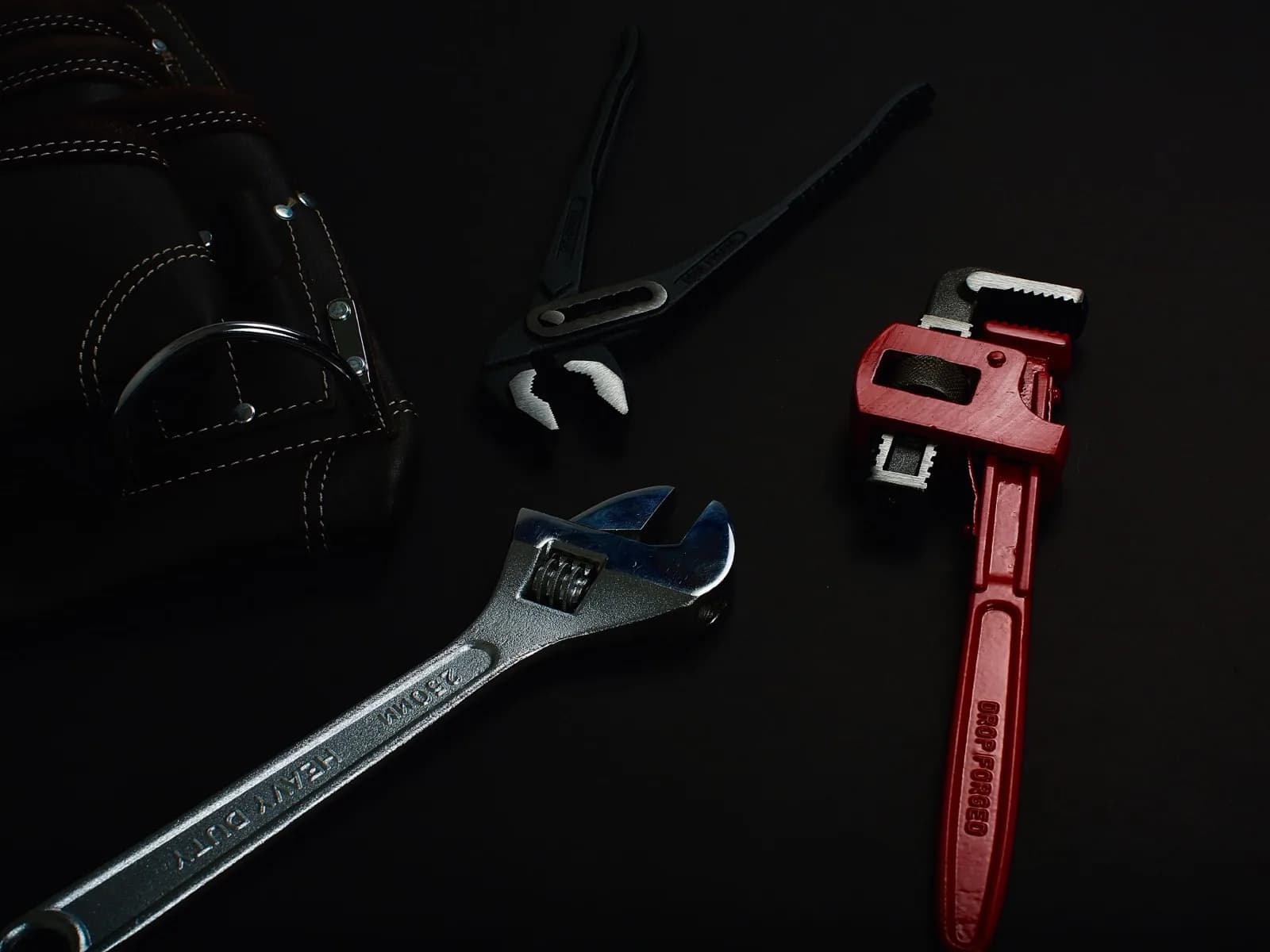Pipe wrench and assorted hand tools laid out for a plumbing repair