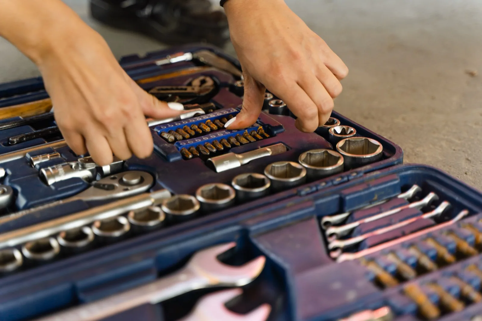 Hand reaching into a plumber's toolbox organized with sockets and hand tools