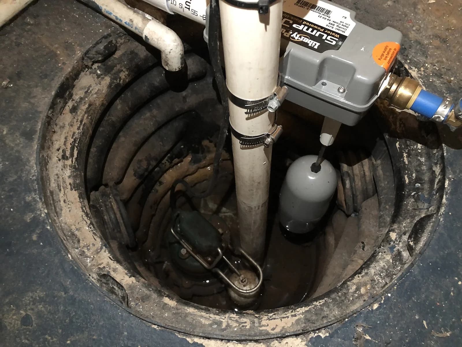 Basement sump pit installation with discharge piping, check valve, and float switch visible