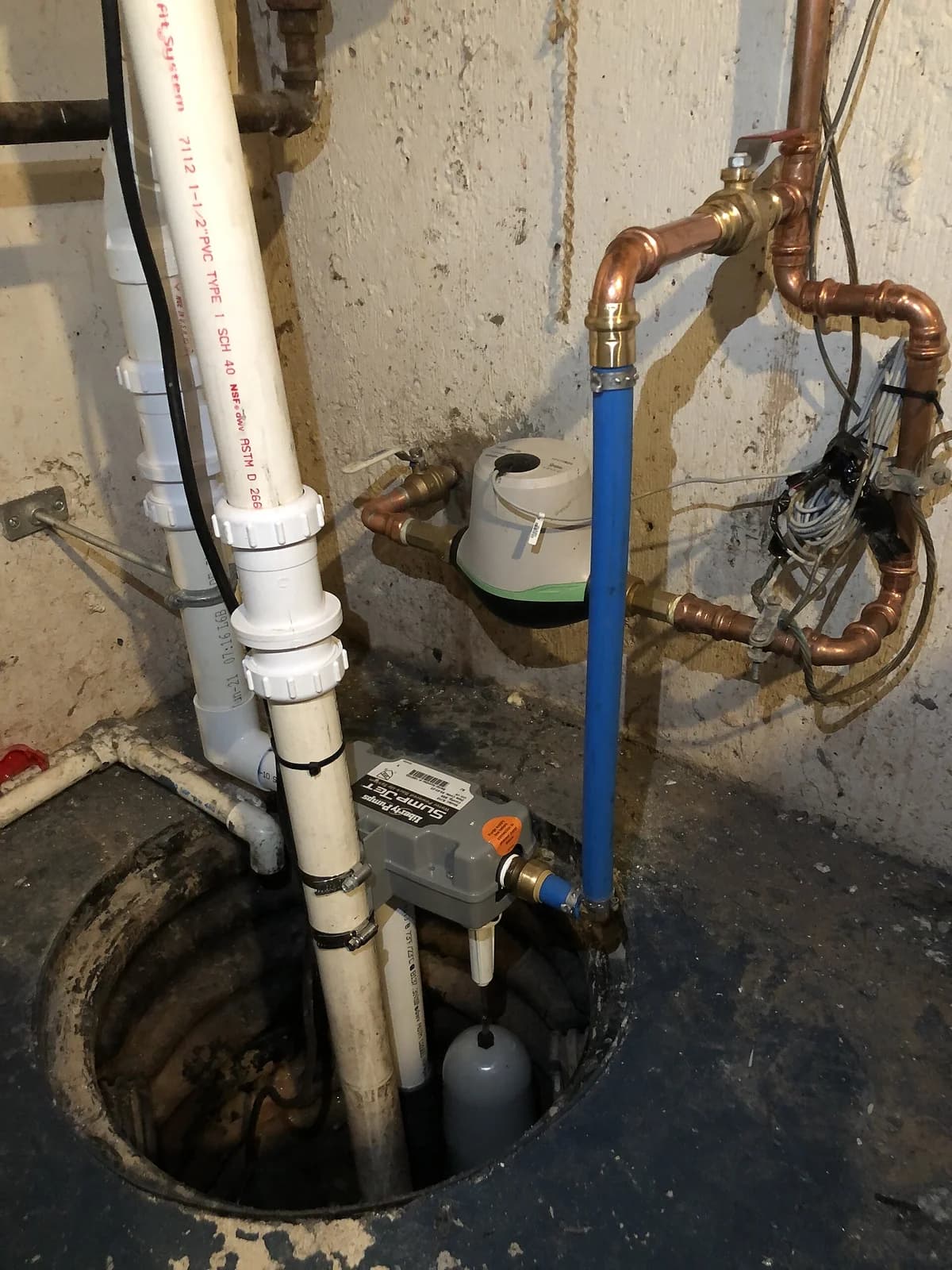 Newly installed sump pump in a basement sump pit with PVC discharge pipe and float switch