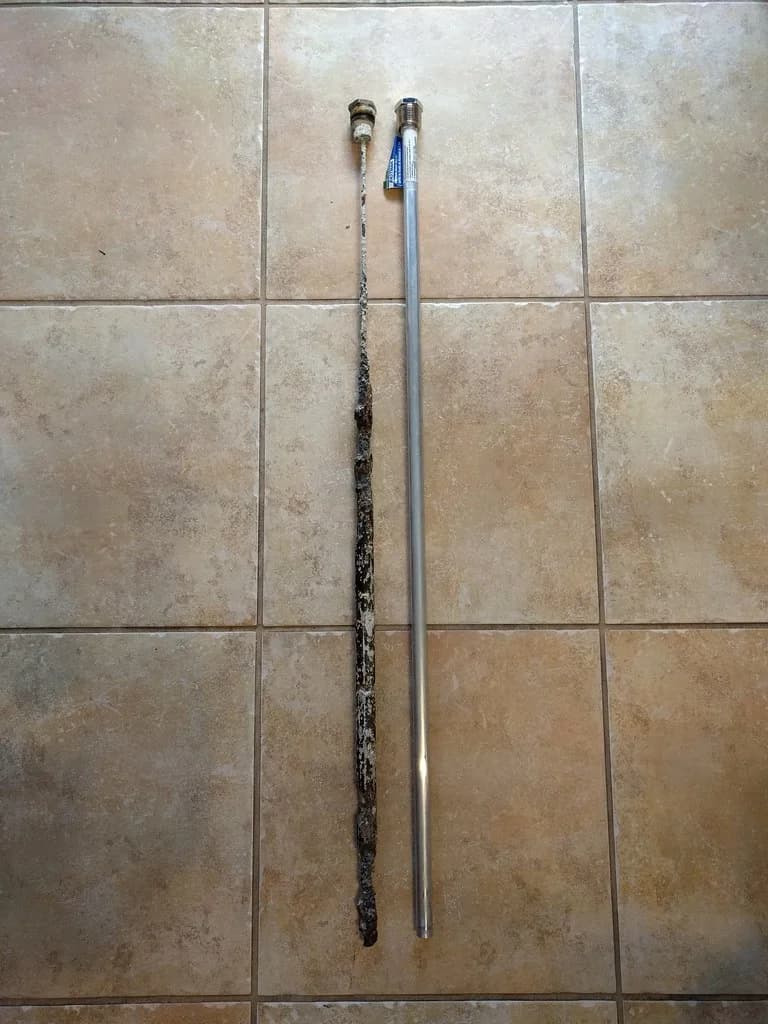 Heavily corroded water heater anode rod next to a new replacement rod