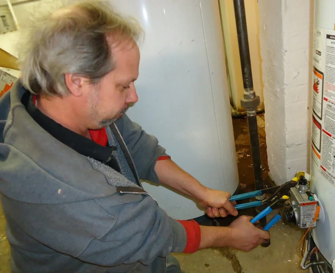 Plumber using two wrenches to tighten a fitting at a water heater's gas control valve