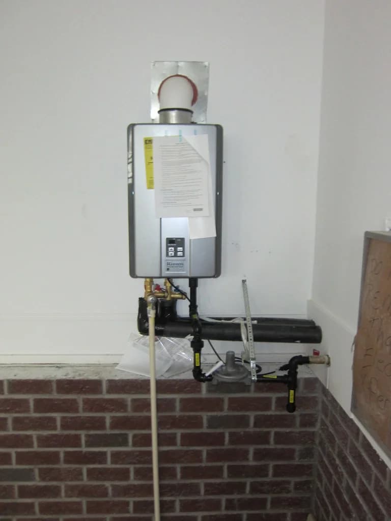 Wall-mounted gas tankless water heater with vent pipe and gas and water connections below